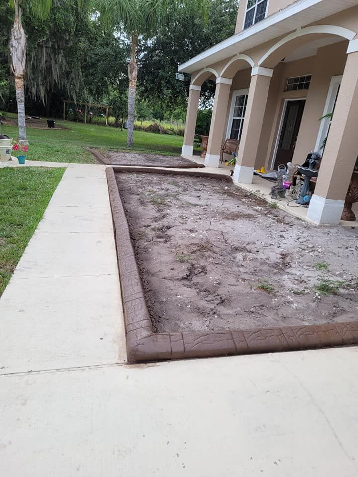 A concrete walkway leading to a house with a dirt area in front of it.
