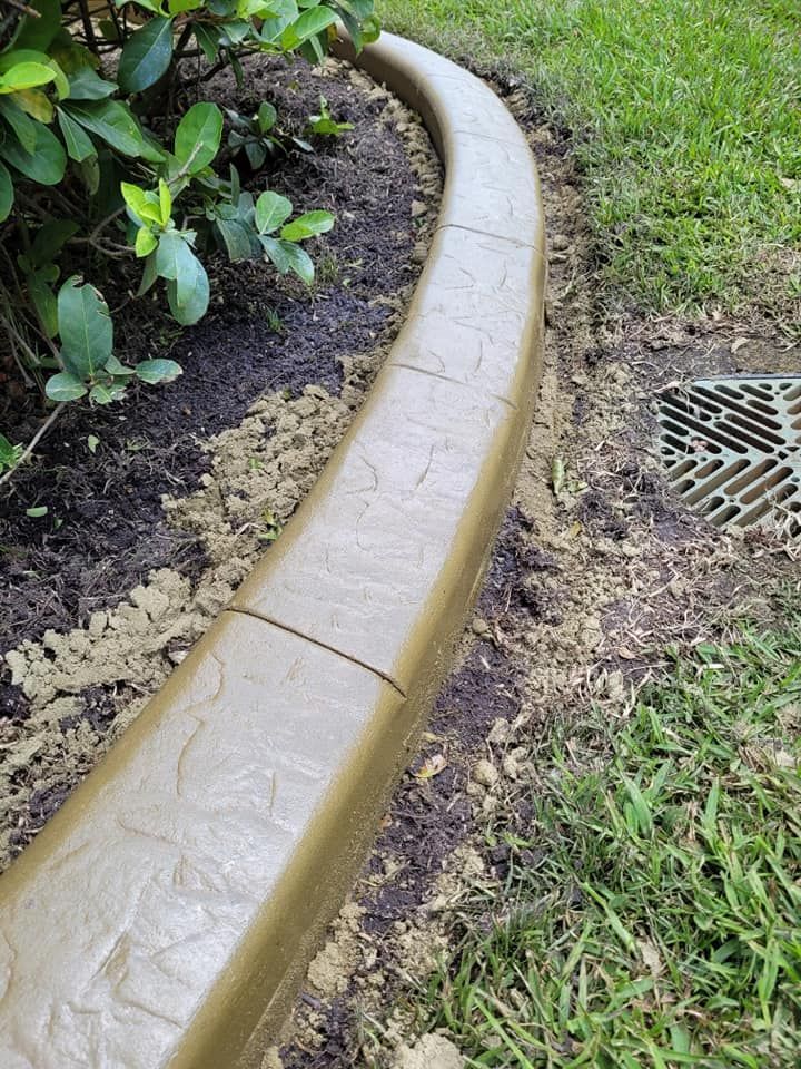 A concrete curb is sitting on top of a lush green lawn next to a drain.