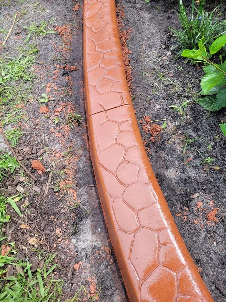 A brick curb is sitting in the dirt next to a grassy area.