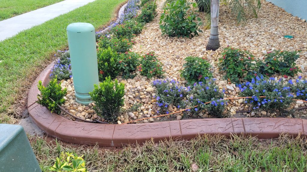 A garden with flowers , shrubs , and a green pipe in the middle of it.
