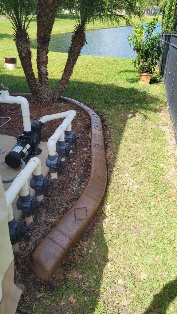 A pool pump is sitting on top of a concrete curb next to a pond.