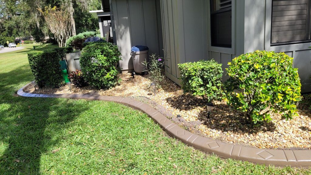 A lawn with a concrete curb and bushes in front of a house.