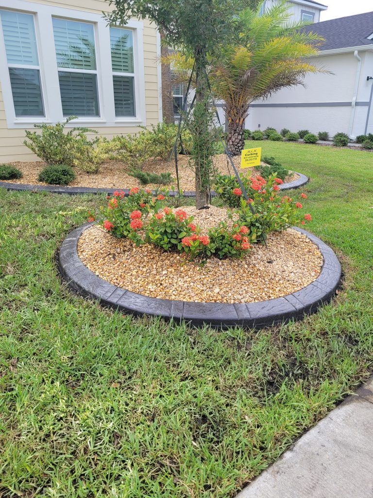 A circular garden in the middle of a lush green lawn in front of a house.