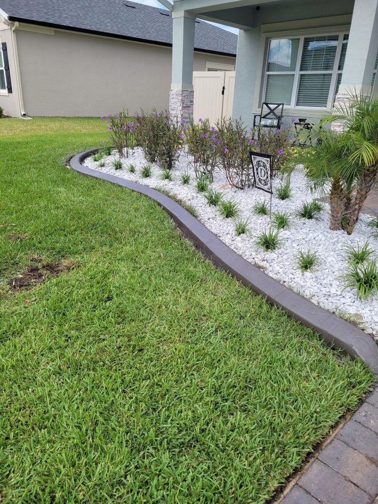 A lush green lawn with a concrete curb and white gravel in front of a house.