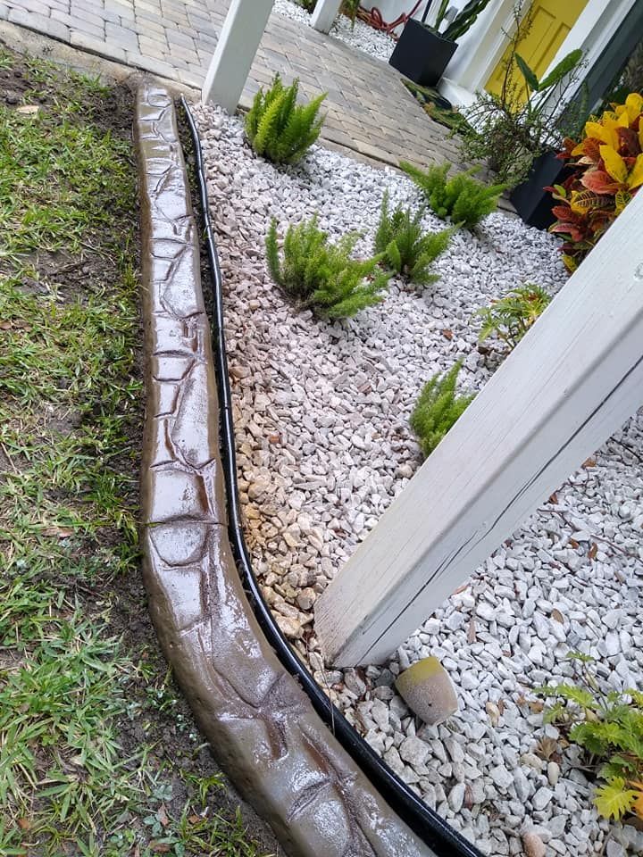 A concrete curb is surrounded by gravel and plants in a garden.
