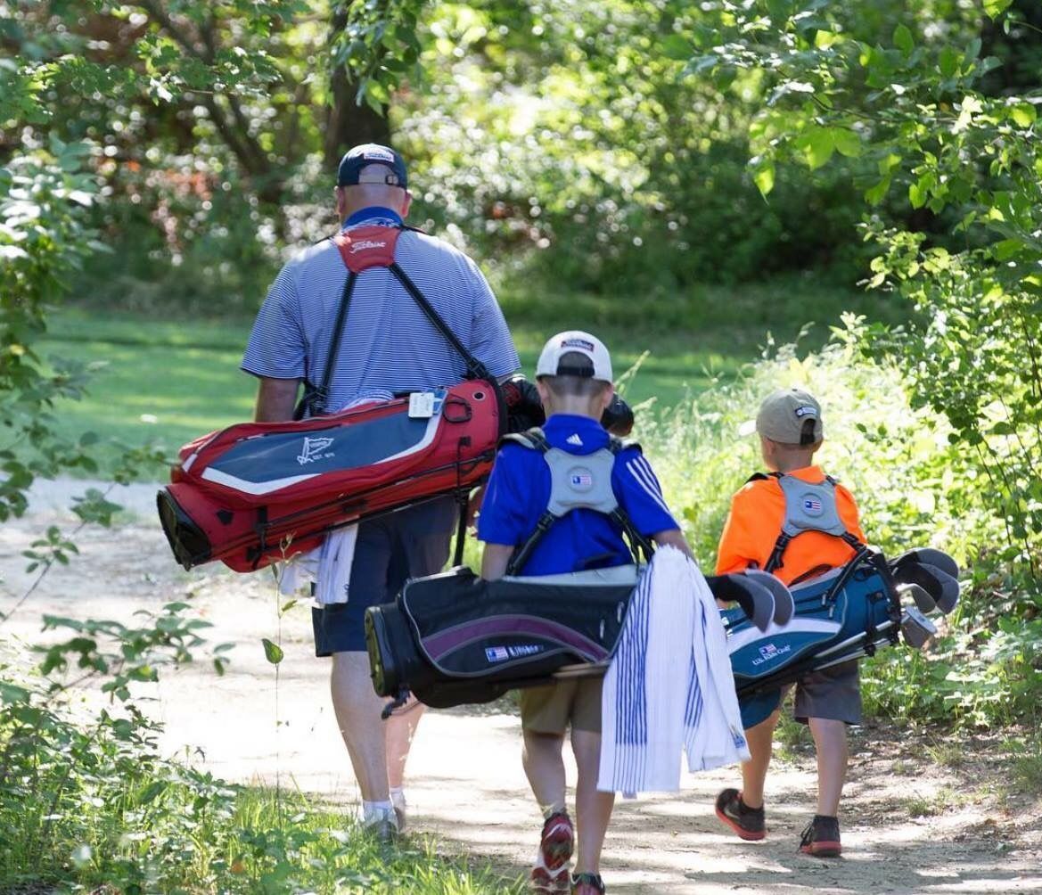 A man and two boys are walking down a path carrying golf bags.