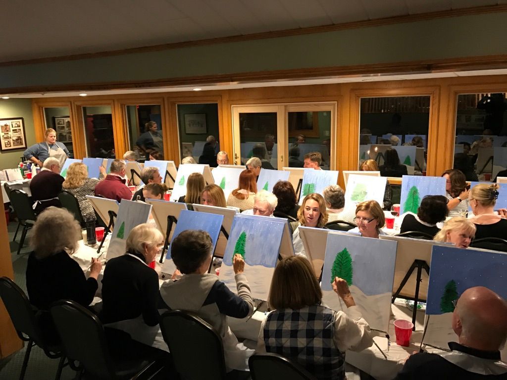 A group of people are sitting at tables painting trees.