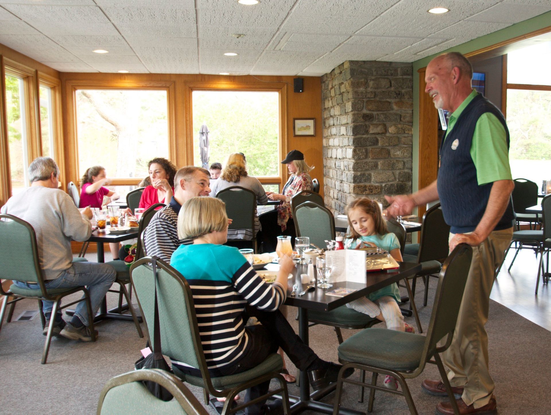 A man is talking to a group of people sitting at tables in a restaurant.