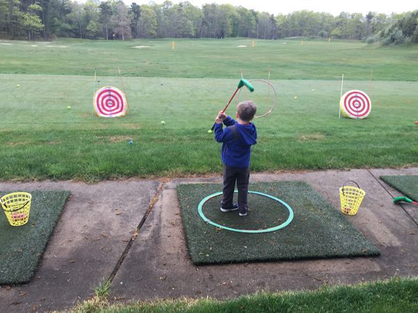 A young boy is swinging a golf club at a target on a golf course.