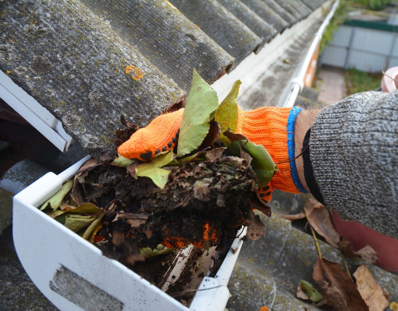 man cleaning a clogged roof gutter from dirt, debris and fallen leaves