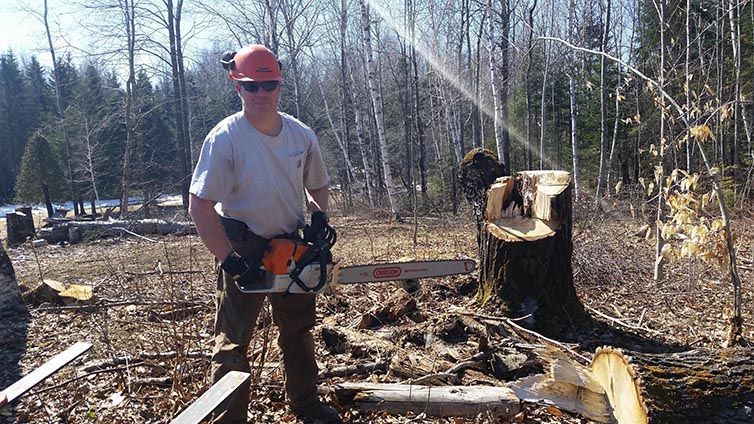 A man is standing in the woods holding a chainsaw.