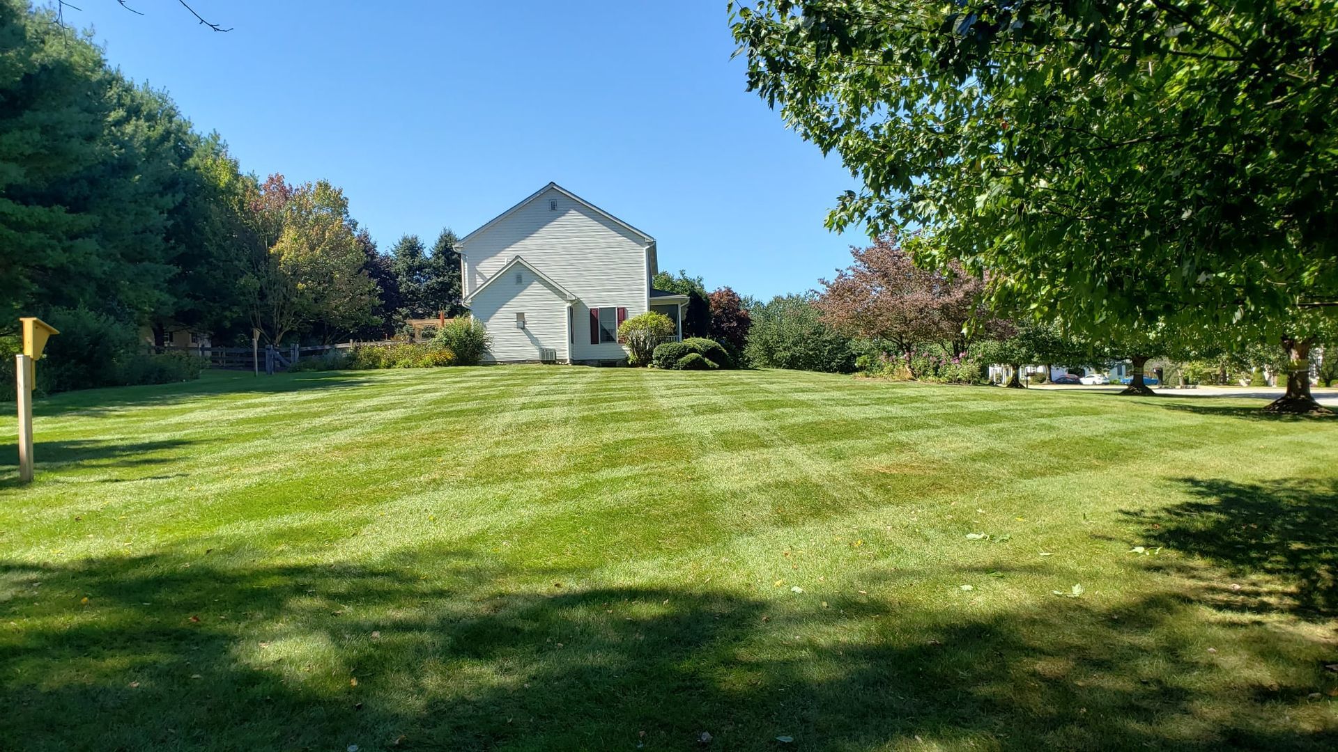 A large lawn with a house in the background and trees in the foreground.
