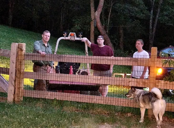 Three men and a dog are standing behind a wooden fence.