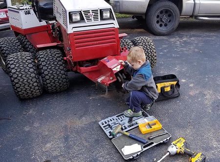 A little boy is working on a tractor in a parking lot