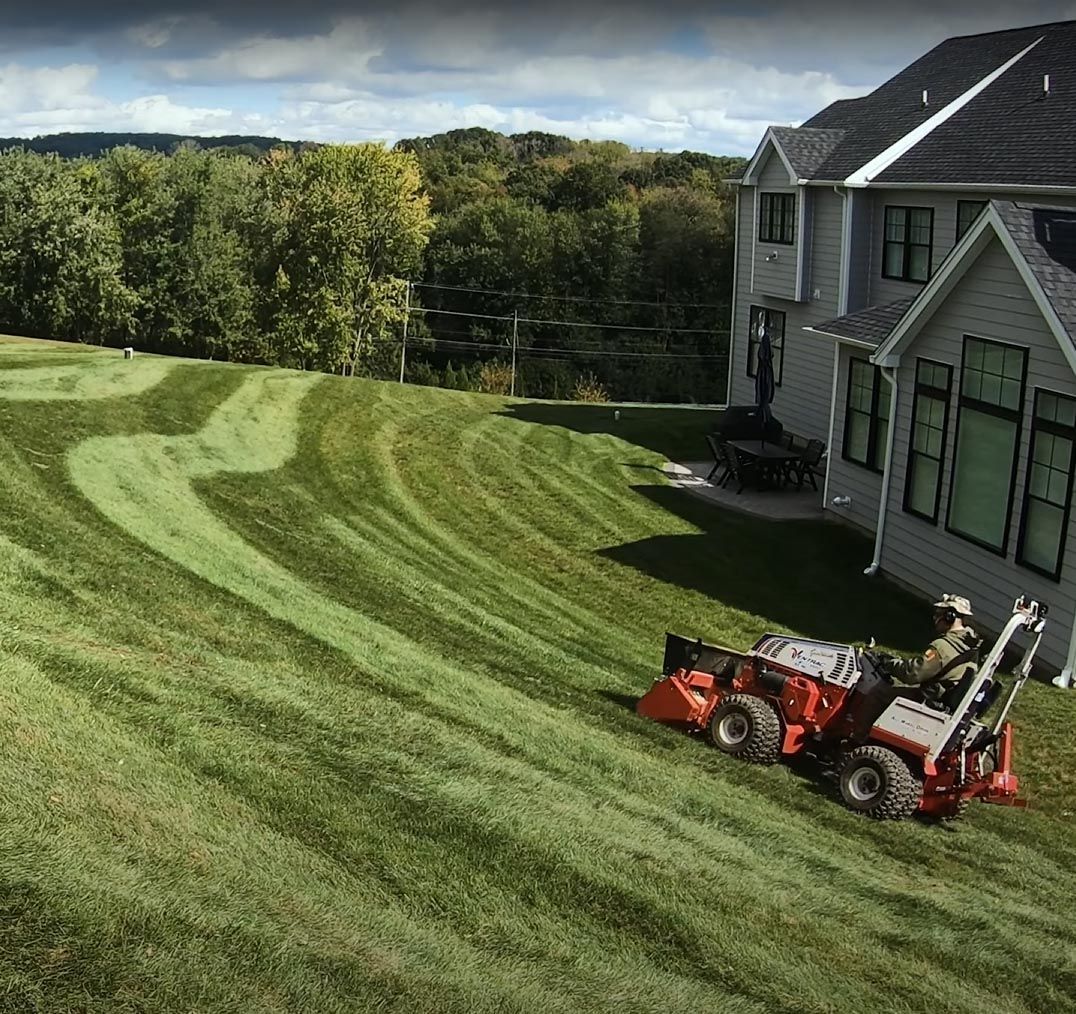 A man is mowing a lush green lawn in front of a house.