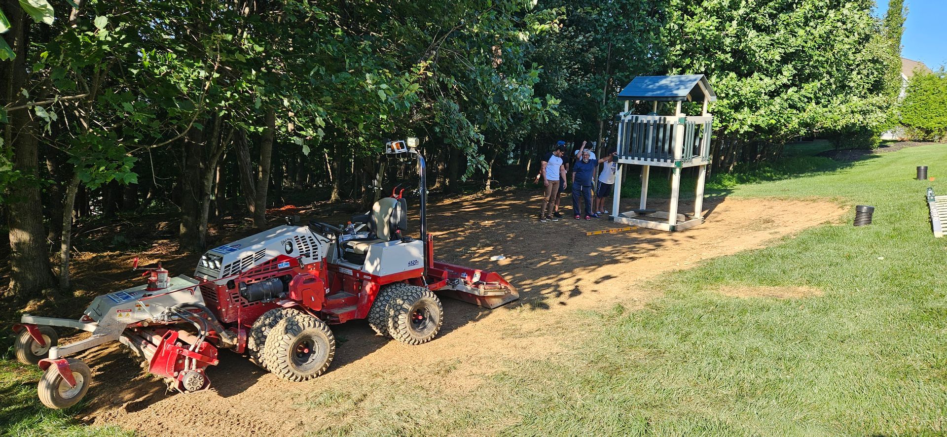 A red tractor is parked in a yard next to a playground.