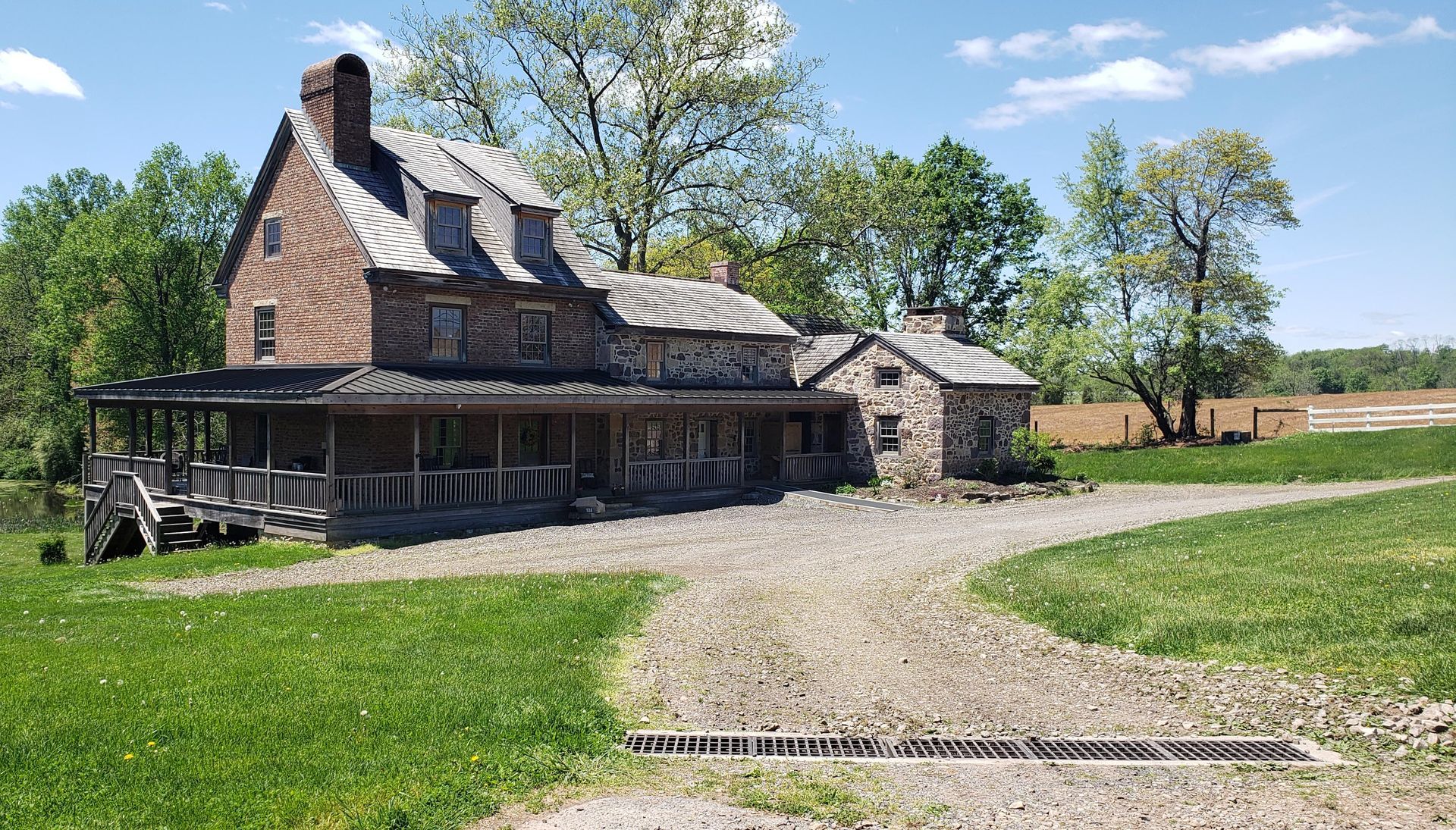 A large brick house with a porch in the middle of a grassy field.