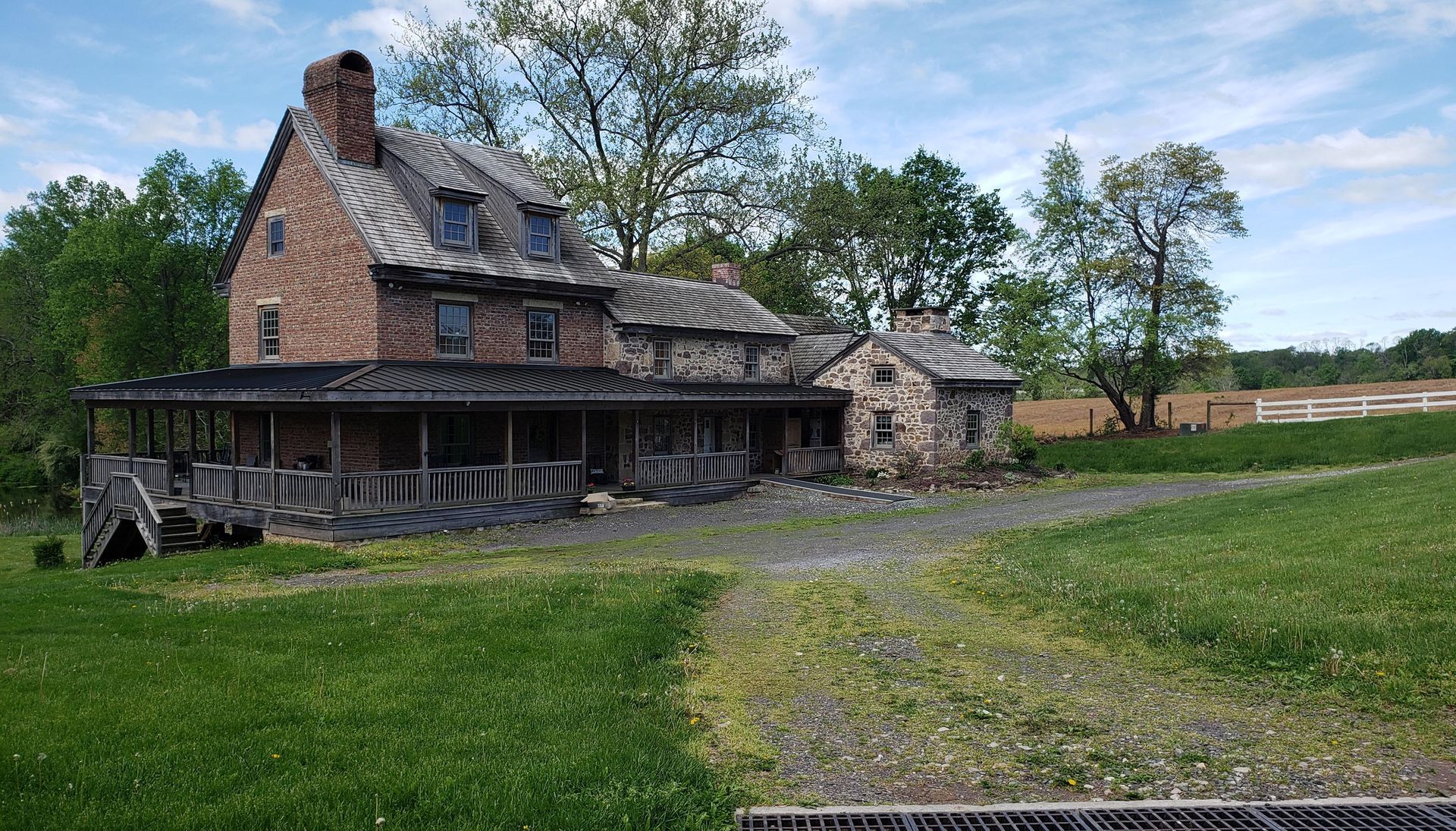 A large brick house with a porch is sitting in the middle of a grassy field.