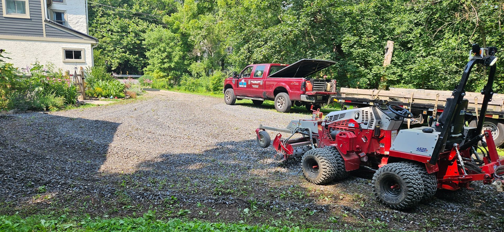 A red tractor is parked in a gravel lot next to a truck.