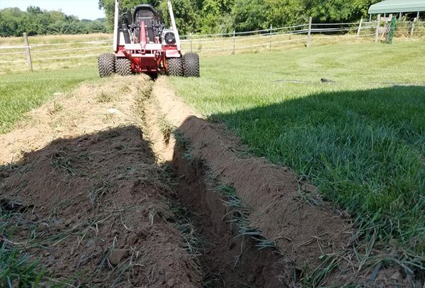 A tractor is digging a trench in the grass.
