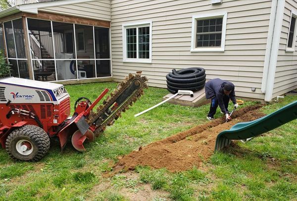 A man is digging a trench in the backyard of a house.