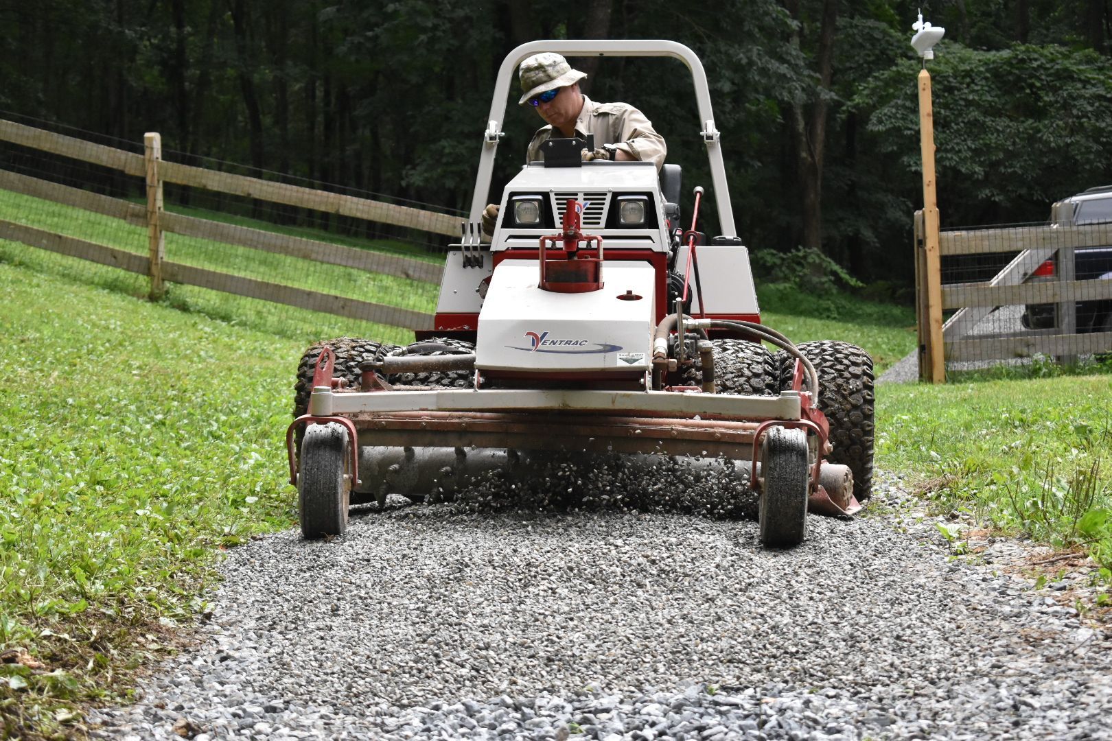 A man is driving a lawn mower on a gravel road.
