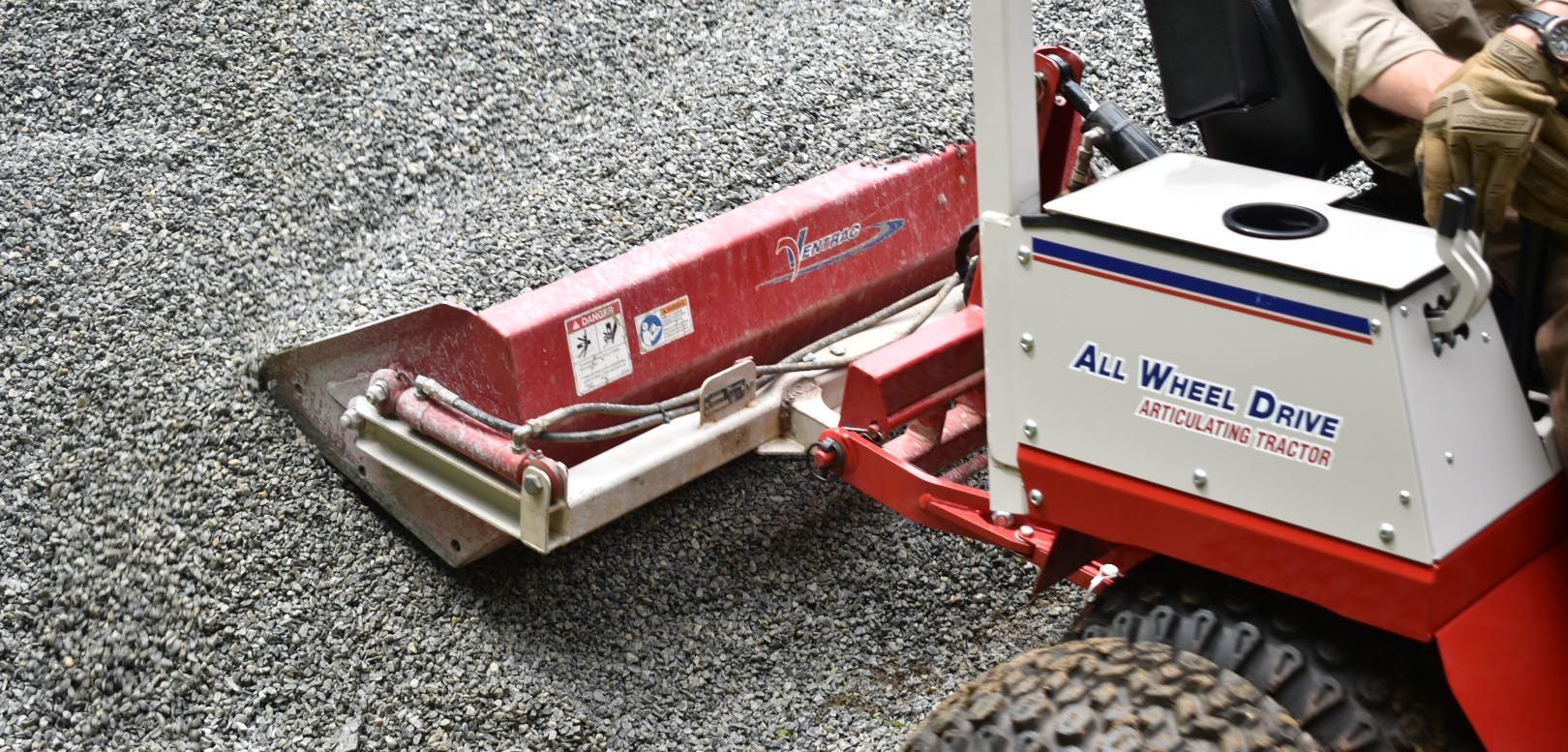 A person is driving an all wheel drive tractor on a gravel road.