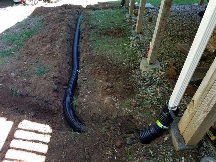 A black pipe is laying in the dirt next to a wooden post.