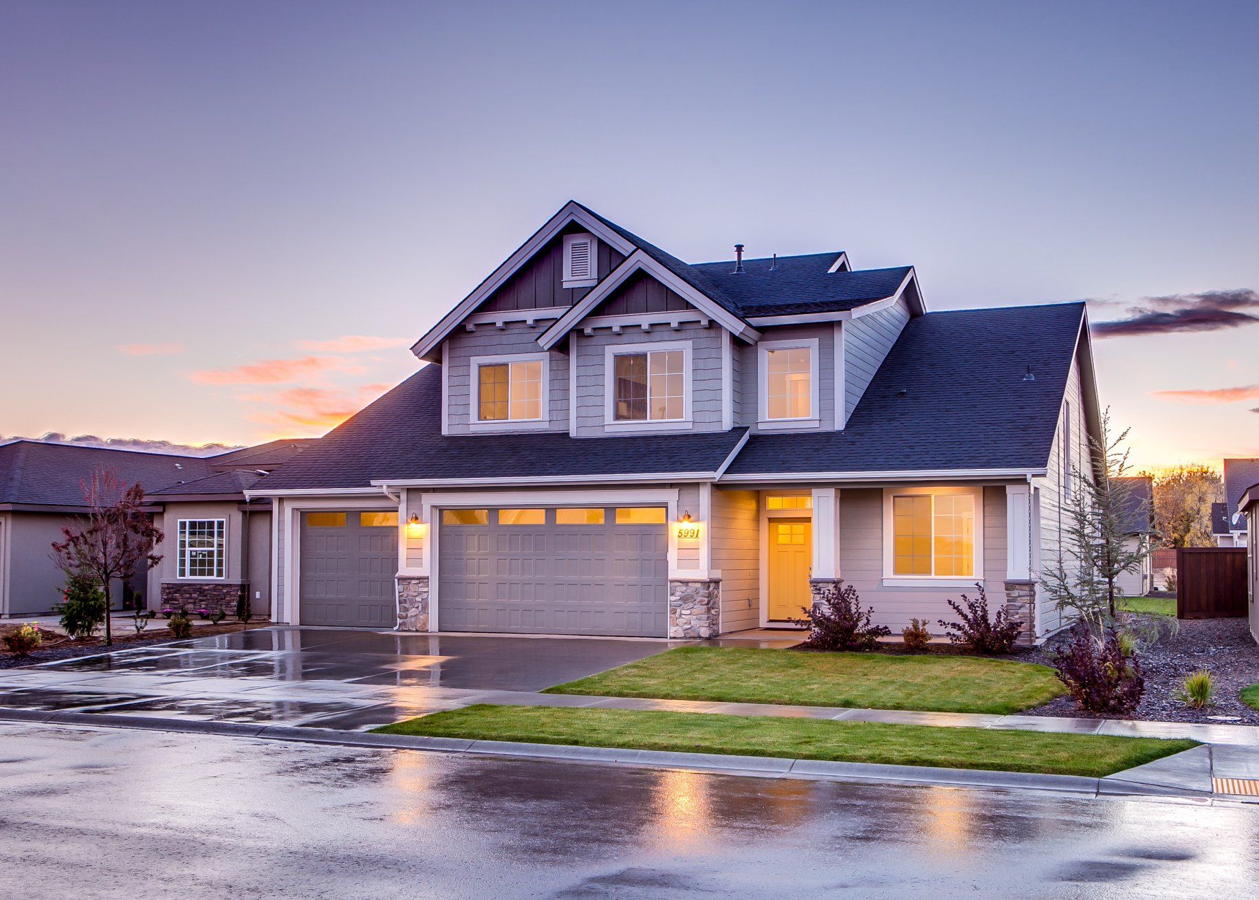 A large house with a garage and a driveway on a rainy day.