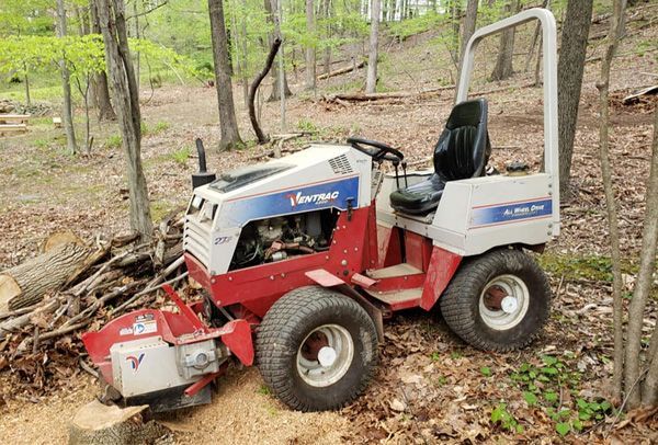 A lawn mower is parked in the woods next to a tree stump.