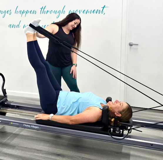 Kirsty Mueller Pilates Instructor assisting a client exercising on a Pilates Reformer machine