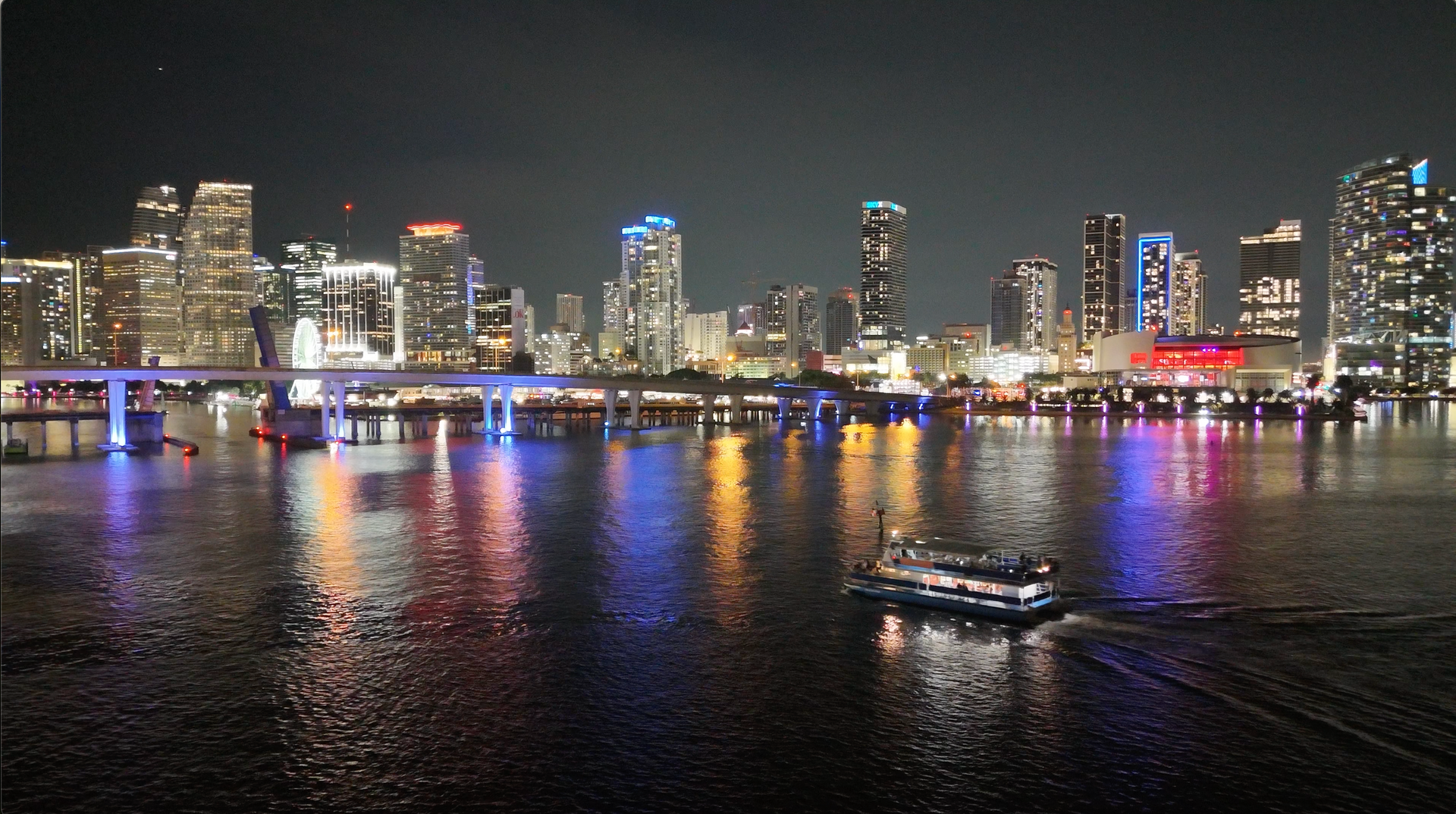 Miami Night Cruise passing Downtown skyline with glowing buildings and reflections on the water