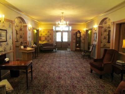 A dimly lit, traditional hotel lobby with patterned carpeting, arched wall alcoves, wooden furniture, and a chandelier.