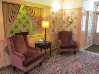 Two velvet chairs sit on a floral rug in a room with light wood paneling, a small side table, and floral wallpaper.