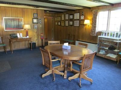A wood-paneled room with a central oval table, four wooden chairs, a side desk with a typewriter, and a glass display case.