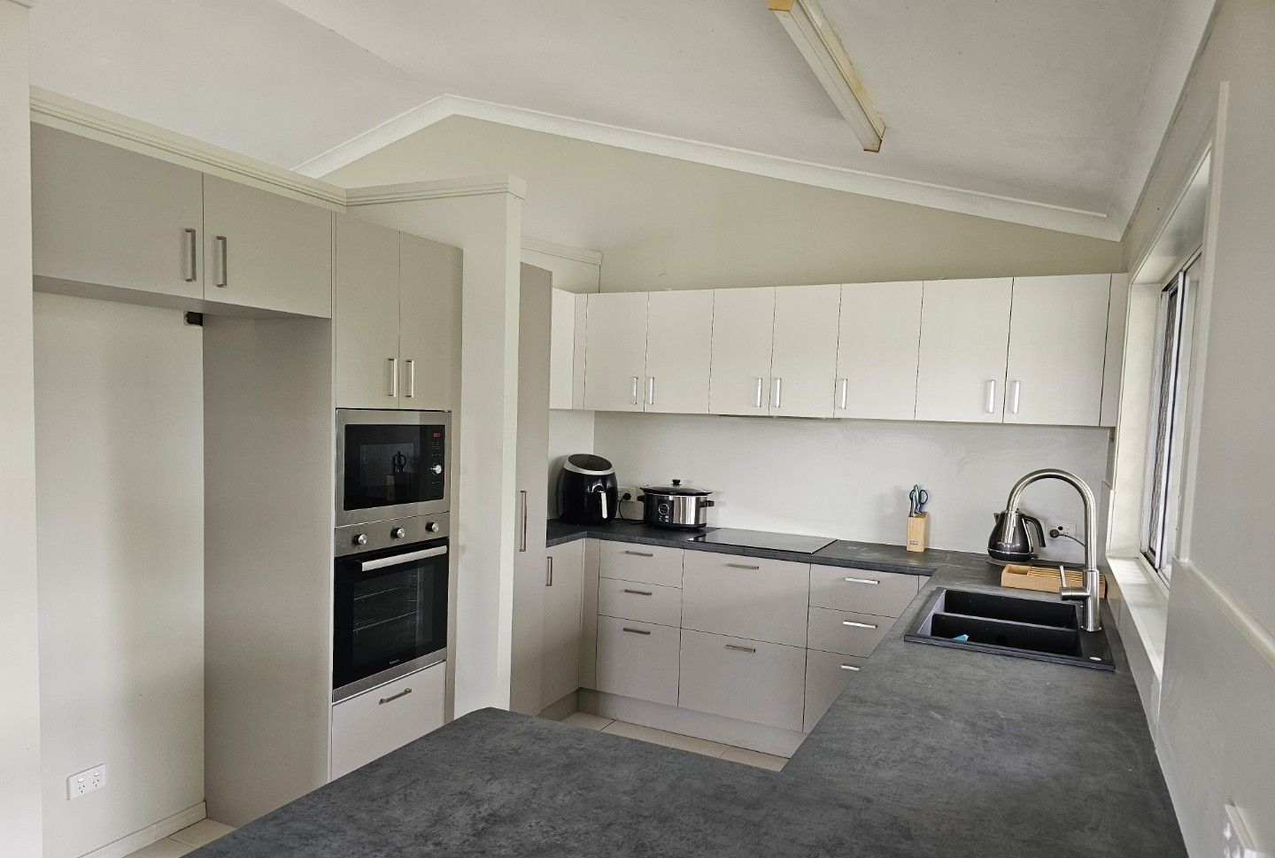 Kitchen With Grey Cabinets, Appliances, Dark Countertops, and a Window — ModulPlus in River Heads, QLD