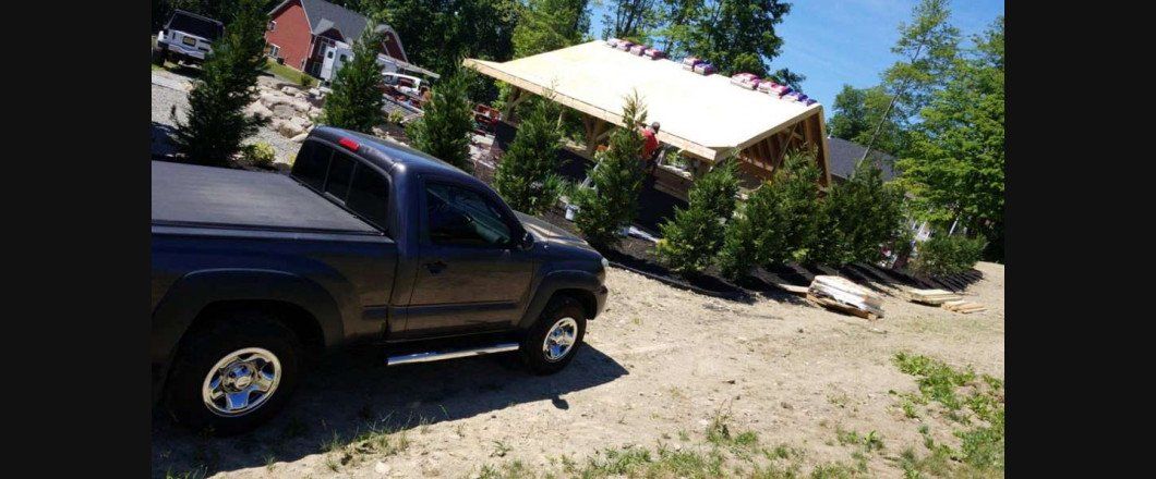 A black truck is parked on a dirt hill in front of a house.