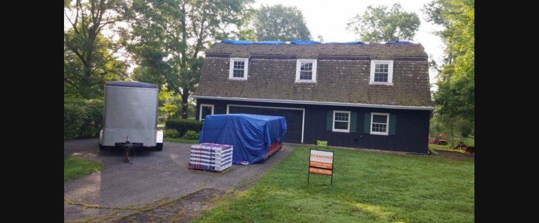 A house with a blue tarp on the roof and a trailer in front of it.