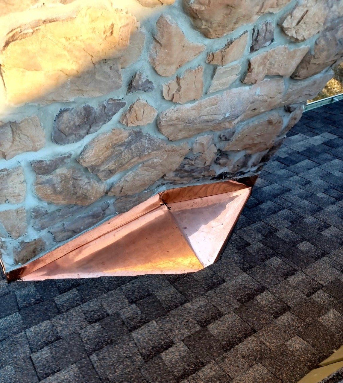 A copper gutter is sitting on a roof next to a stone wall.