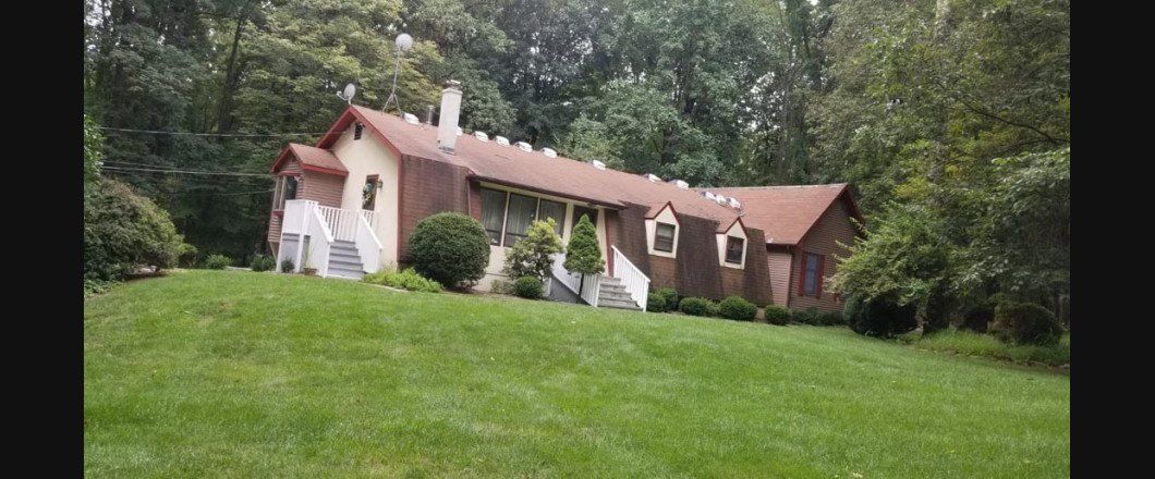 A large house sits on top of a lush green hillside surrounded by trees.