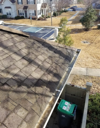 A green trash can is sitting in a gutter on the roof of a house.