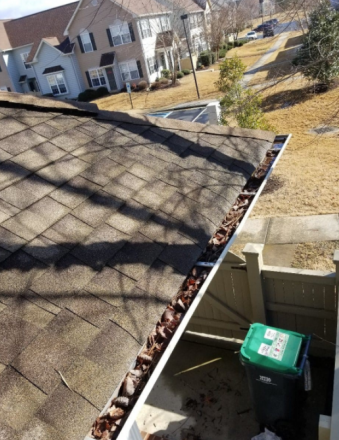 A gutter with leaves on it is on the roof of a house.