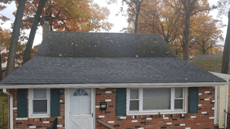 A small brick house with a black roof and green shutters