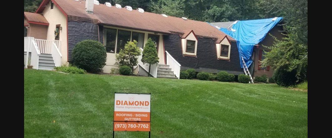 A house with a blue tarp on the roof and a for sale sign in front of it.