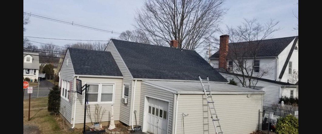 A white house with a black roof and a garage next to it.
