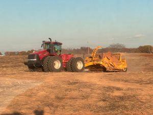 A red Case IH tractor pulling a large yellow pull-behind earth scraper across a dry, brown field.