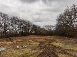 A clearing with muddy tire tracks in the foreground, bordered by a dense line of bare trees under a cloudy sky.
