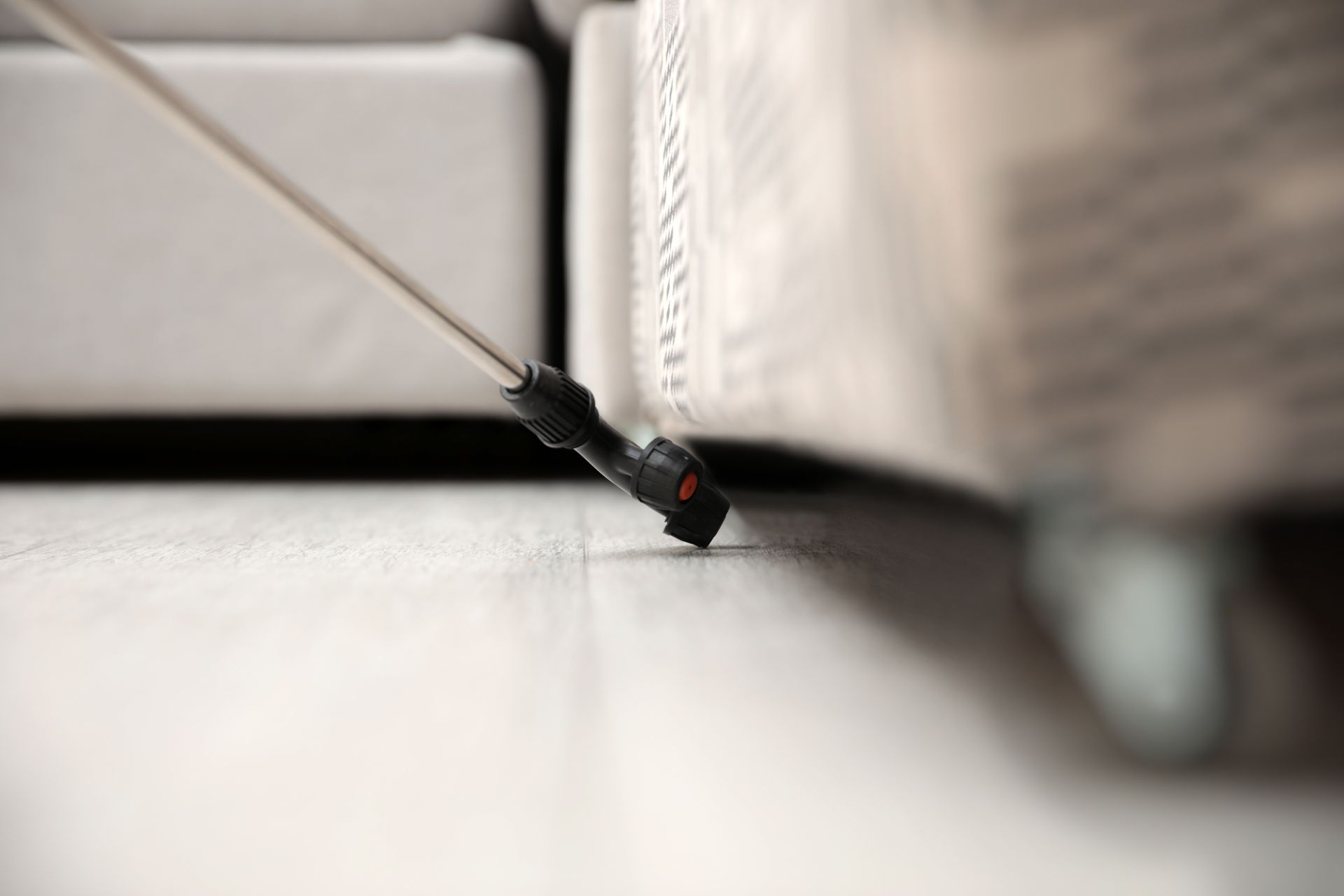 Nozzle spraying insecticide under a white couch.