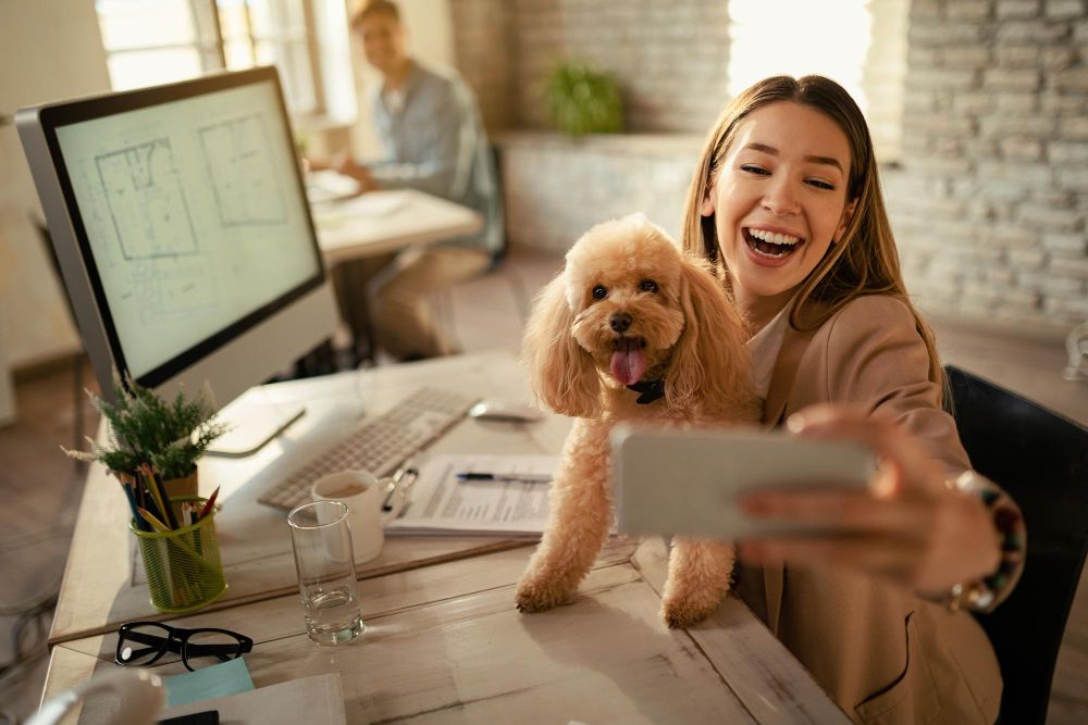 Happy entrepreneur taking a selfie with her dog while working from home office