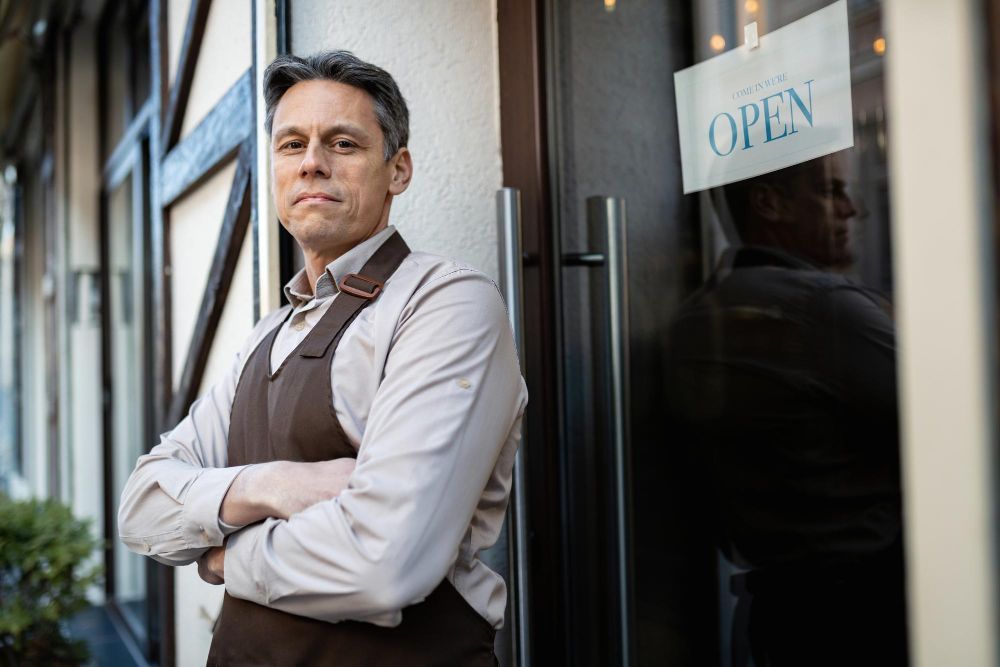 Small business owner standing confidently outside his shop with open sign